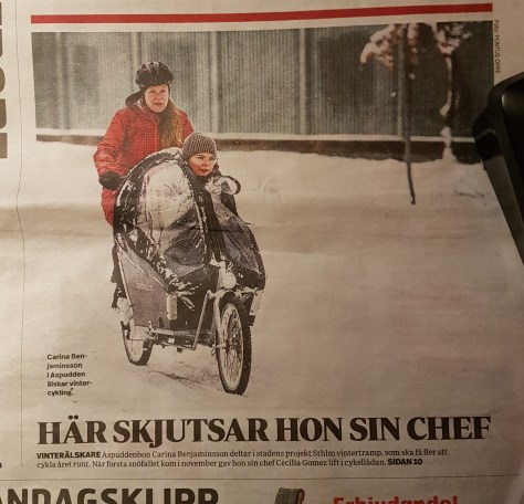 Lokaltidningens hela framsidebild där ledaren i projektet för att cykla hela året runt skjutsar sin chef i en cykelkärra.